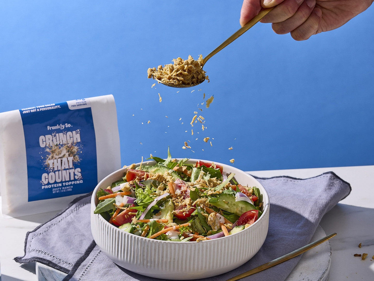 Zesty Ranch protein topping being spooned over a fresh summer salad